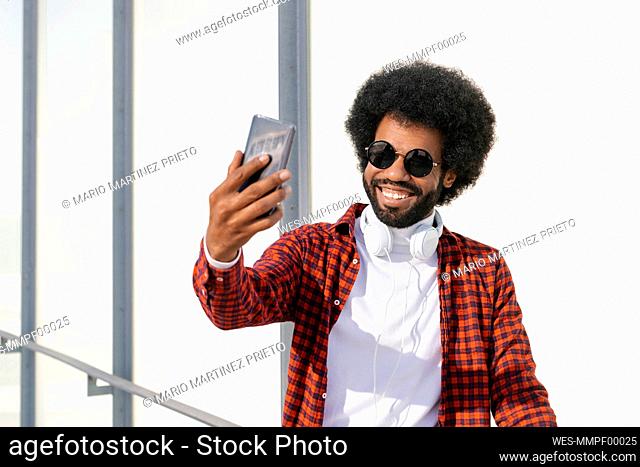 Happy man wearing sunglasses taking selfie through smart phone