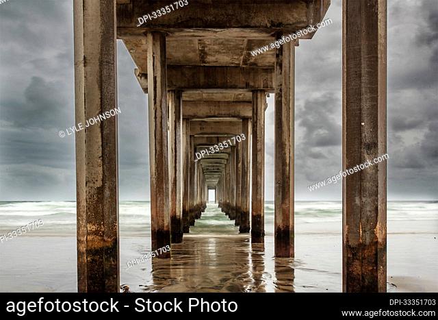 Stormy sky and the repeating view of the cement columns under the iconic Scripps Pier in the Pacific Ocean near San Diego; La Jolla, San Diego County