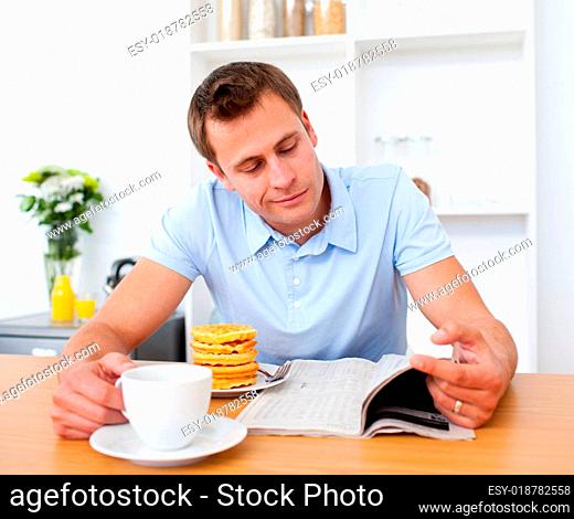 Smiling man reading a newspaper while having breakfast