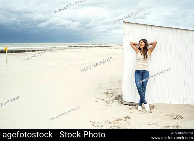 Young woman with hands behind head against beach hut during weekend