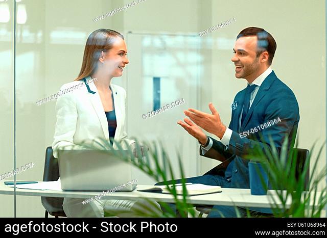 Smiling diverse business partners young man and woman discussing project sitting in a modern bright meeting. Handsome young businessman and a woman cooperating...