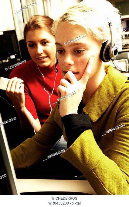 Teenage girl wearing a headset using a computer with another teenage girl sitting beside her
