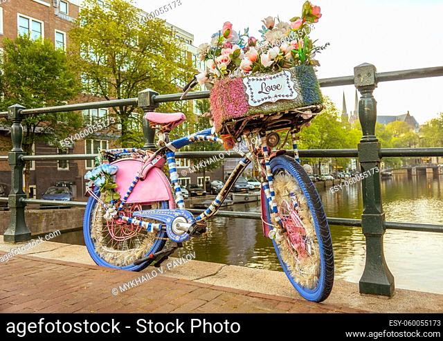 Netherlands. Cloudy morning on the Amsterdam canal. A flower-decorated bicycle with a LOVE sign is parked by the bridge fence