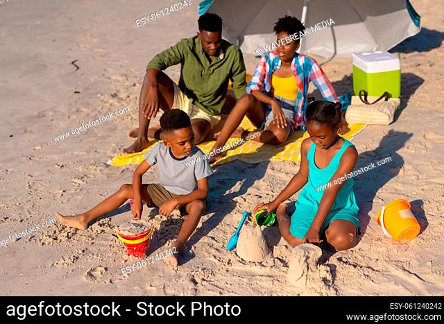 High angle view of african american parents sitting under umbrella while children playing with sand