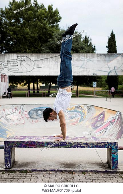 Young man doing a handstand on bench in skatepark