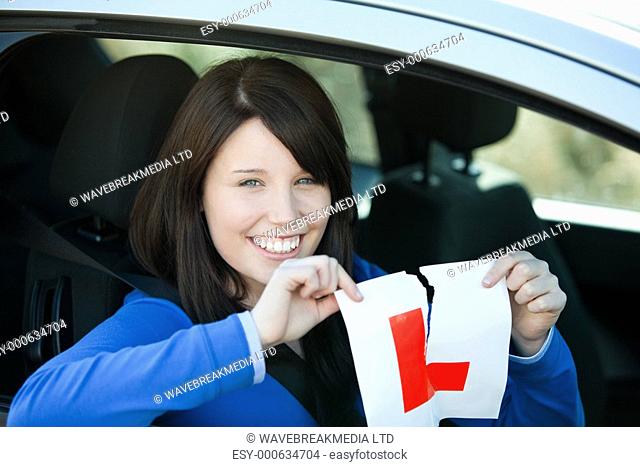 Jolly teen girl sitting in her car tearing a L-sign after having her drivers licence