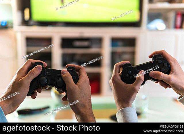 Male friends hands playing video game at home