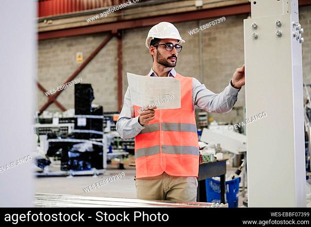 Engineer with blueprint operating machinery at industry