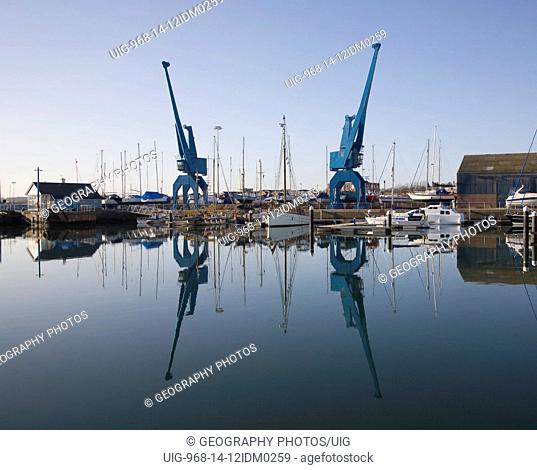 Two large blue industrial cranes reflected in water of Wet Dock marina, Ipswich, Suffolk, England