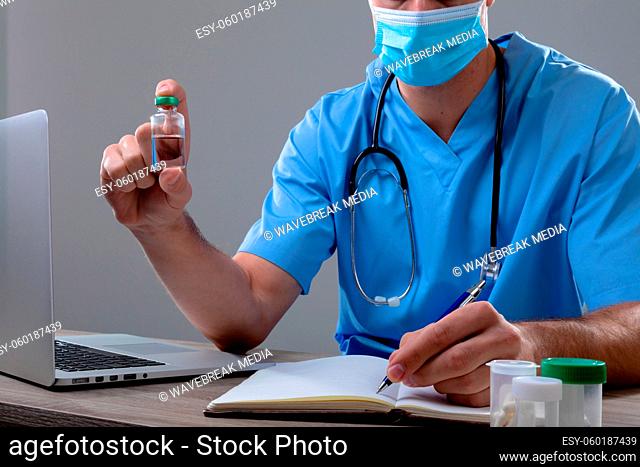Caucasian male doctor wearing face mask holding vaccine vial