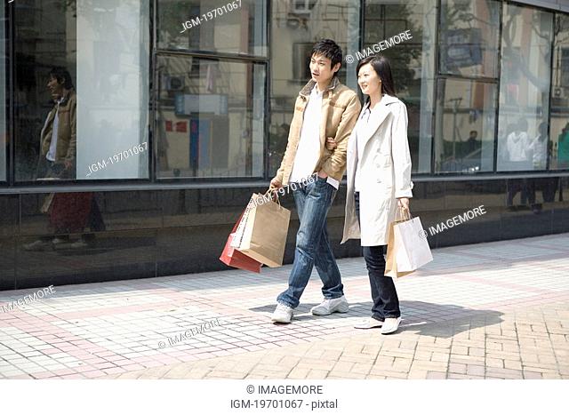 Young couple walking on street with shopping bags, smiling