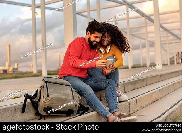 Happy man and woman using smart phone on steps at sunset
