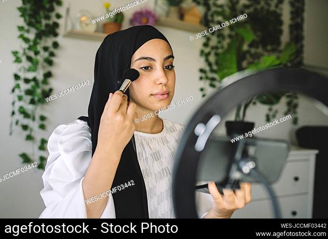 Female vlogger applying blush while showing makeup tutorial at home