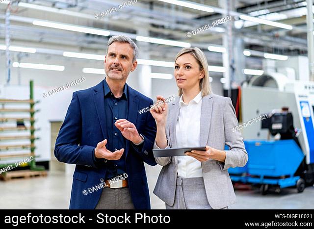 Businesswoman with digital tablet and businessman talking in factory