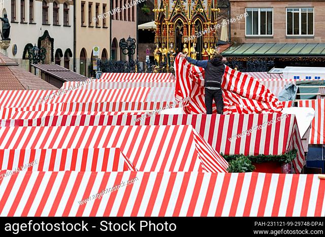 21 November 2023, Bavaria, Nuremberg: A man places the red and white striped roof tarpaulin on a stand during set-up work at the Nuremberg Christmas Market