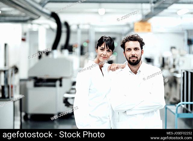 Male and female scientists in white lab coats standing at bright laboratory