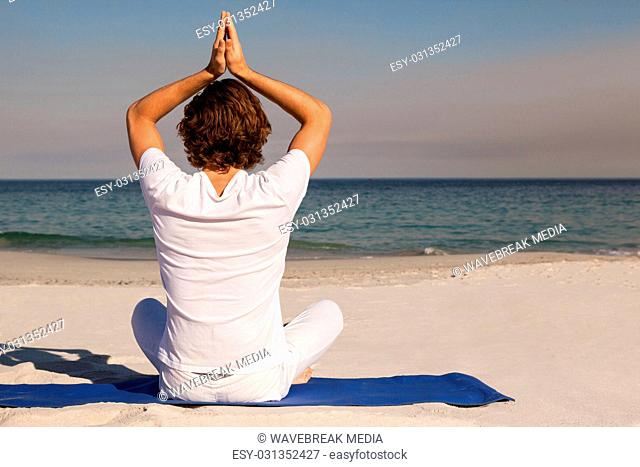 Man performing yoga at beach on sunny day