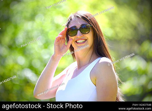 Pretty long-haired young woman (30 years old) in a white top and sunglasses smiles and looks into the camera. Model released! | usage worldwide
