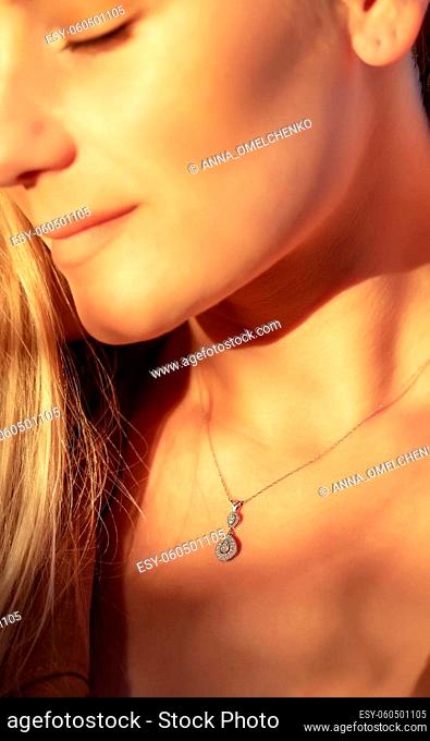 Woman with a Beautiful Pendant on her Neck in Mild Sunlight. Golden Chain with Little Precious Stone. Luxury Jewelry