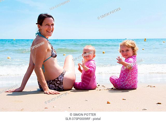 Mother sitting on beach with daughters