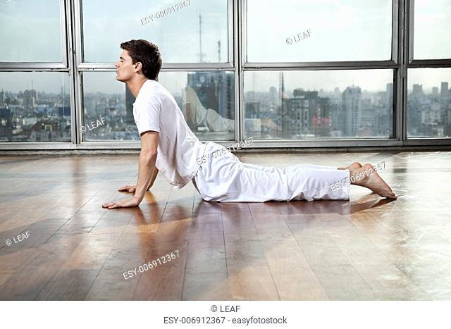 Side view of a young man doing Upward Facing Dog pose at gym