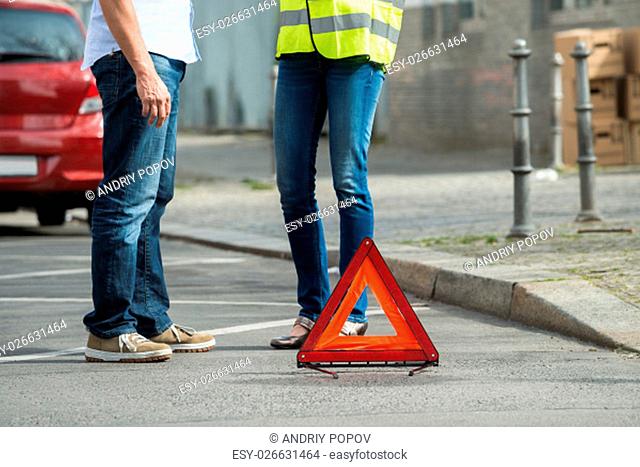 Couple Standing Near Triangular Warning Sign With Broken Down Car