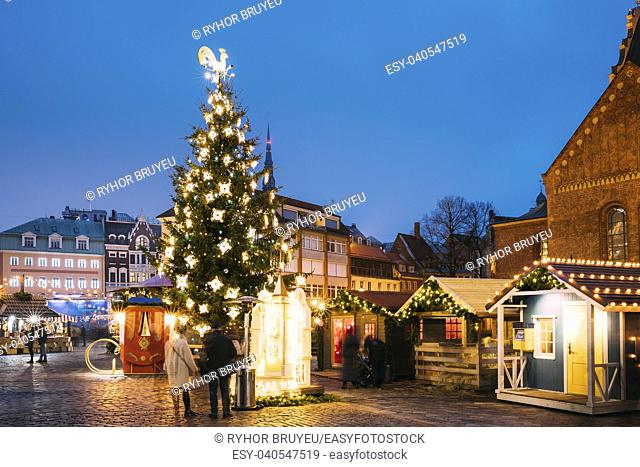 Riga, Latvia. Xmas Market On Dome Square. Christmas Tree And Trading Houses. Famous Landmark In Winter Evening Night In Illuminations Festive Lighting