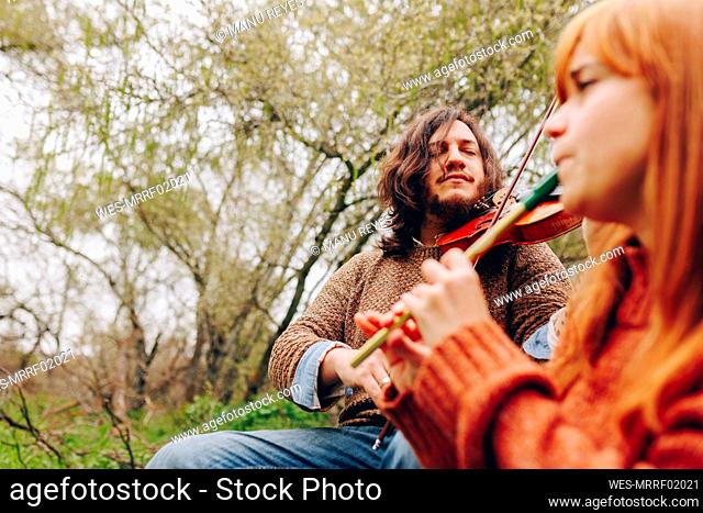 Concentrated man playing violin with woman in field