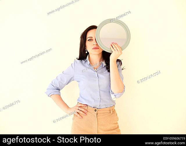 Brunette female in summer dress standing with round mirror on white background in studio