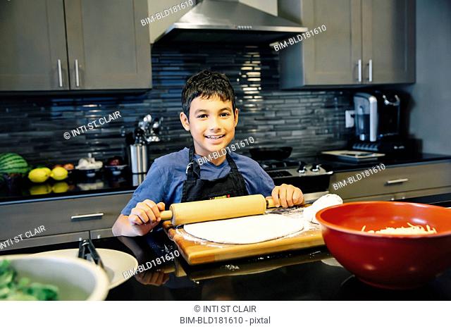 Mixed race boy rolling dough in kitchen