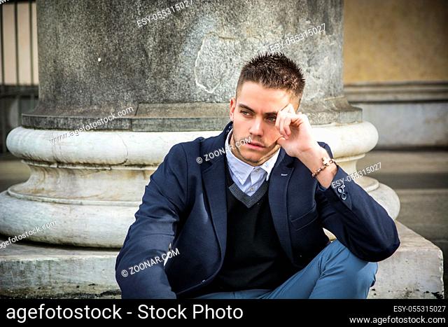 Handsome young man outdoor wearing jacket and shirt sitting by historic building in European city. Turin, Italy