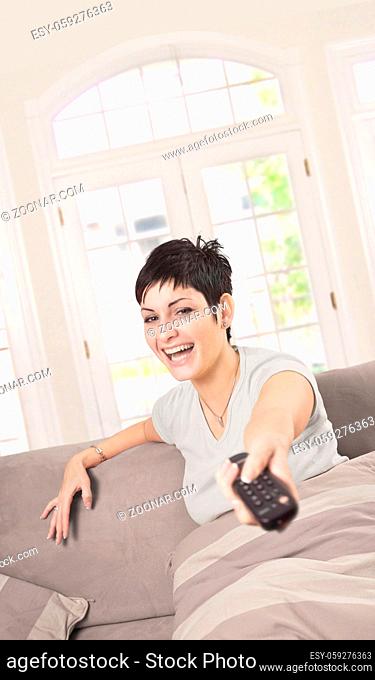 Young woman is wathing TV at home in the living room with a remote controller in hand