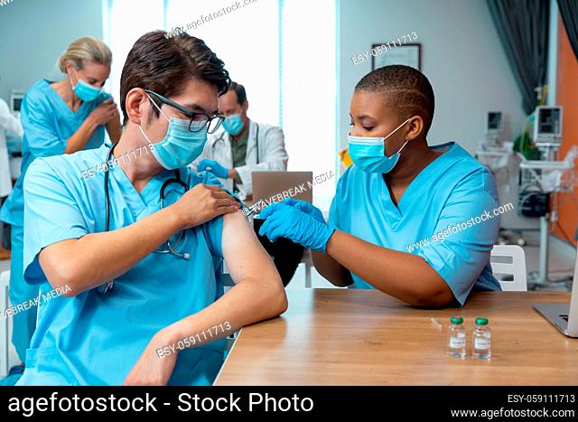 African american female doctor giving covid vaccination to male colleague, both in face masks