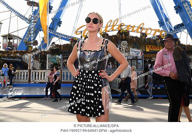 27 September 2019, Bavaria, Munich: The artist and performance-art actress Stella Bossi wears a transparent dirndl in front of the ferris wheel on the Wiesn