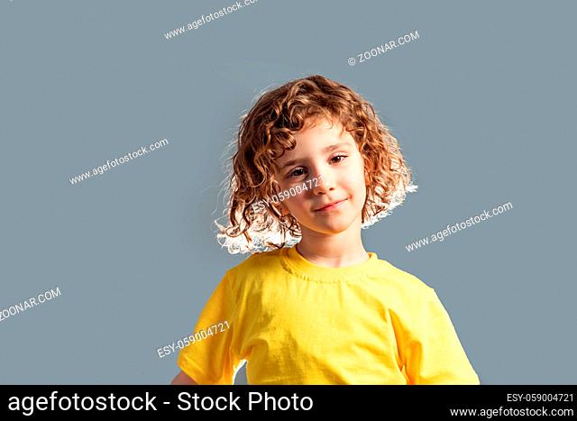 Adorable 5 year kid in yellow t-shirt posing on gray background