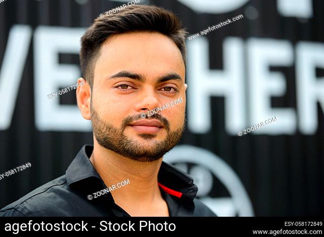 Portrait of young handsome bearded Indian businessman in the city outdoors