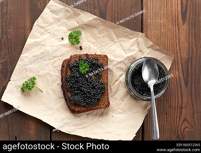 paddlefish caviar, a slice of bread and a jar on a piece of brown paper, top view