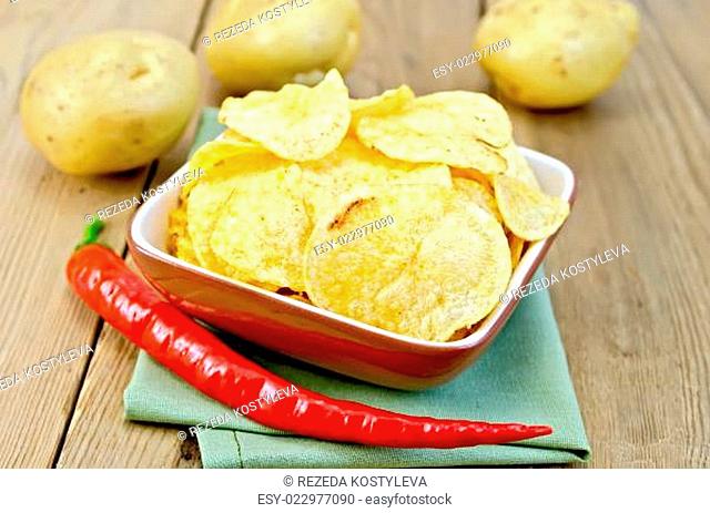 Chips in a bowl with hot peppers and potatoes on board