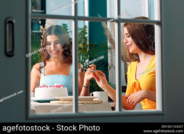 Women happy friends at home sitting and smiling with white birthday cake behind glass door