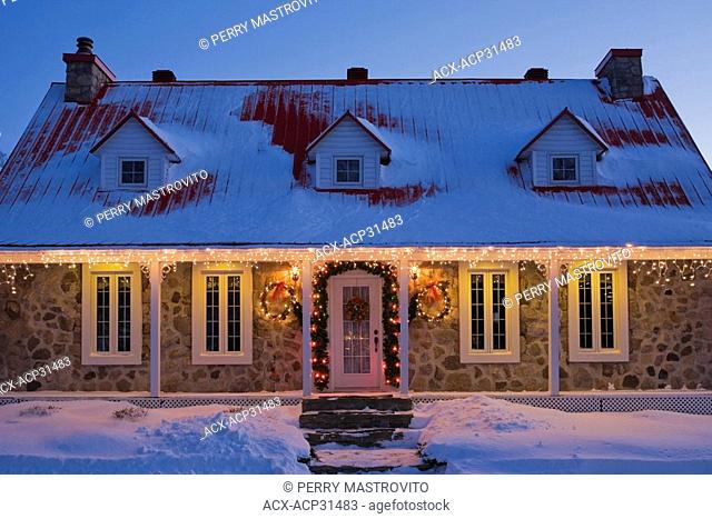 Illuminated two-storied Canadiana style residential home decorated with a Christmas wreath and lights at dusk, Laval, Quebec, Canada