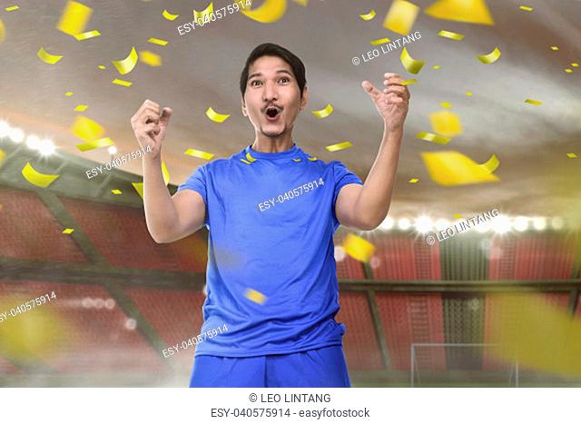 Joyful asian football player man with excited expression on stadium
