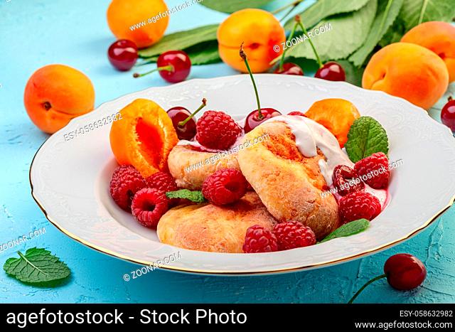 Delicious breakfast - cottage cheese fritters, cottage cheese pancakes with raspberries, cherries, apricots and cream sauce in a white plate, selective focus