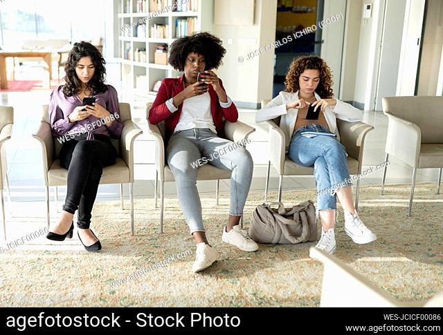 Multiracial businesswomen using smart phone sitting on chair at office