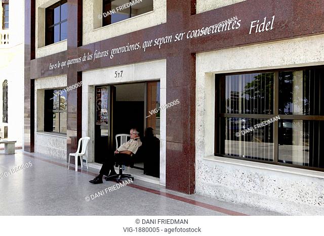 CUBA, HAVANA, 06.07.2009, An on duty security guard sleeps in front of the headquarters of the Communist Youth Party building below a quote from Fidel CASTRO