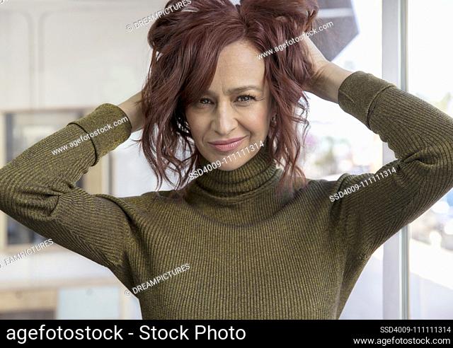 Portrait of a middle-aged woman looking into camera with both her hands up in her hair