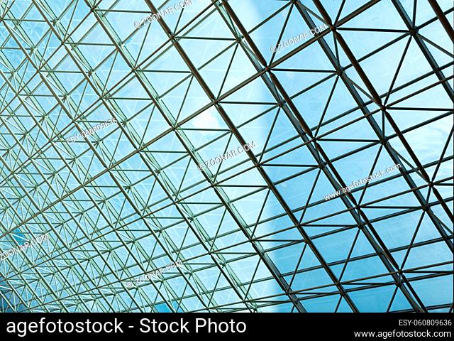 Contemporary steel structure and transparent glass roof revealing blue sky with light clouds