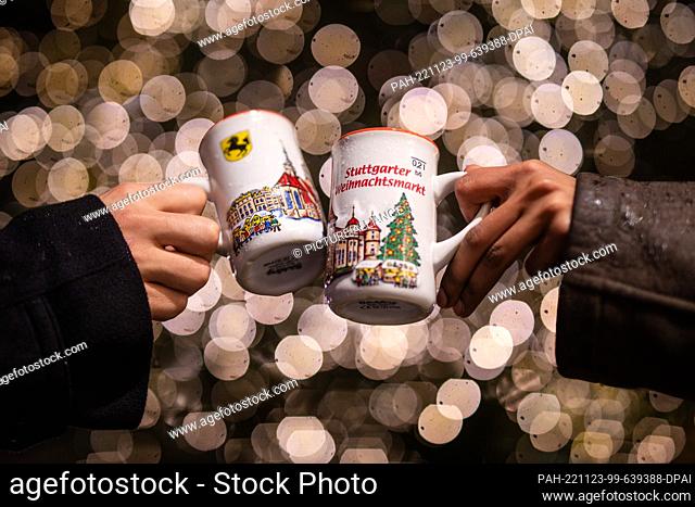 23 November 2022, Baden-Wuerttemberg, Stuttgart: A young woman and a young man toast with their mulled wine cups at the Stuttgart Christmas market