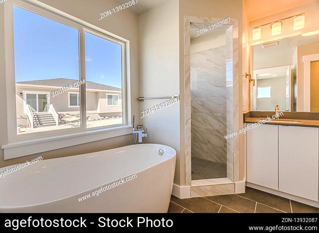 Bathroom interior with bathtub glass door shower and vanity area. The large glass window offers a relaxing view of peaceful blue sky on a sunny day