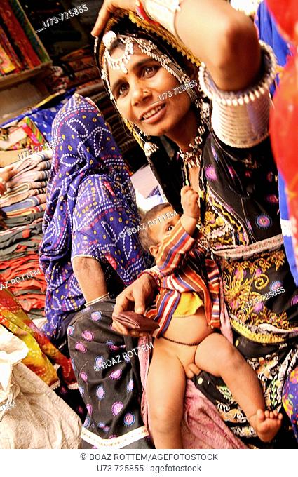 A colorful Rajasthani woman breastfeeds her baby in the local Naguar market, Rajasthan, India