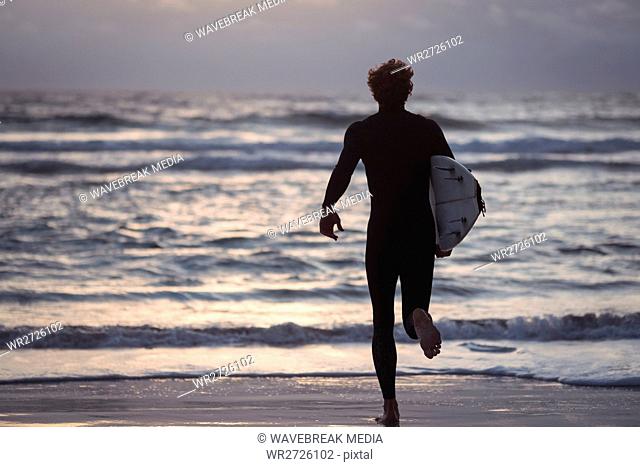 Man carrying surfboard running towards sea
